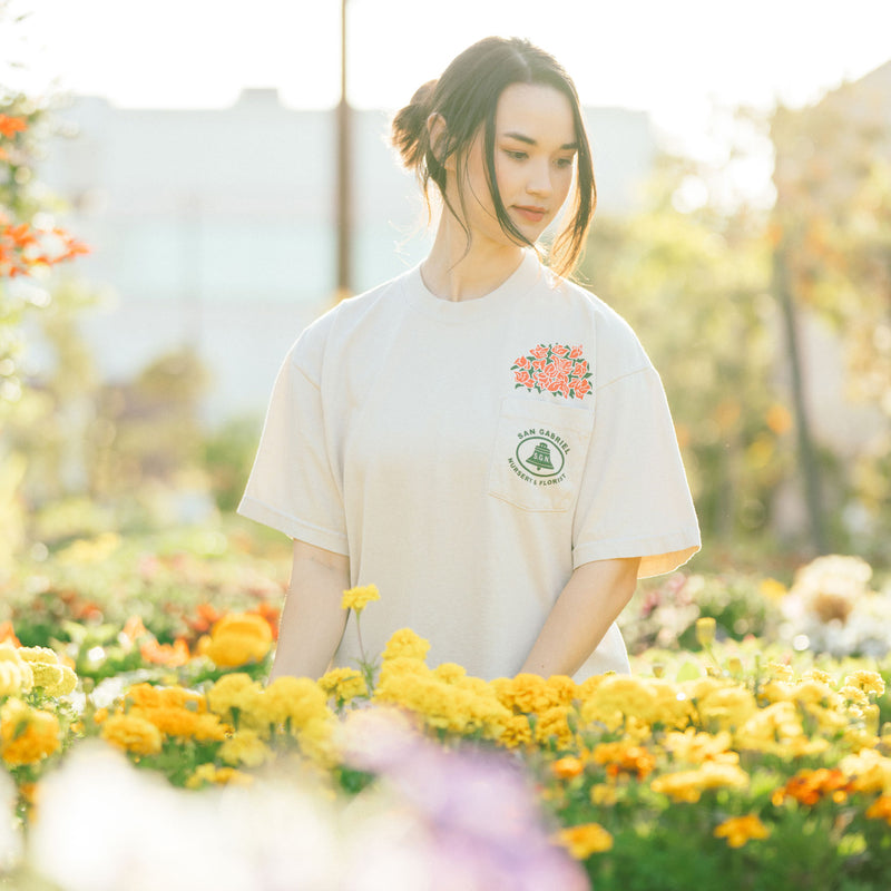 The model, Sarah, wears the Anniversary Pack tshirt. Flowers are in the forefront of the photo. The background is the San Gabriel Nursery, which is celebrating 100 years.